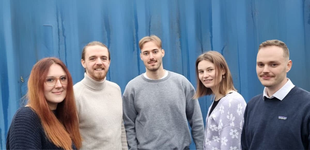 Das Team der Unicorn Factory vor einer blauen Containerwand